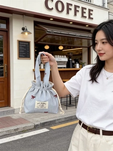 Détail du sac seau en toile rayée bleue avec broderie nœud rouge et fermeture à cordon