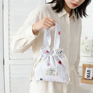 Détail du sac à cordon rayé blanc avec broderie florale et étiquette de marque