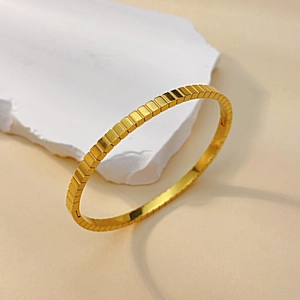 Detailed view of polished golden ice cube geometric bangle on a stone pedestal