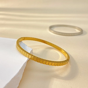Detailed view of luxury gold geometric cube link bracelet on a white textured stone