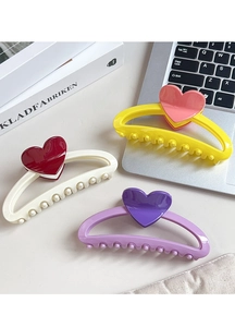 Close-up of three large heart-shaped hair claws in candy colors on a desk setup