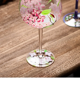 Macro shot of hand-painted pink flowers and green leaves on a crystal red wine glass