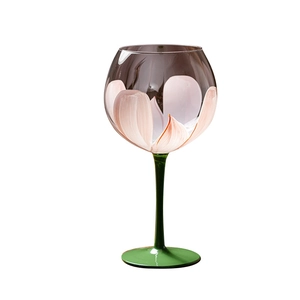Artistic flower-shaped wine glass with pink petals and a contrasting green stem on white