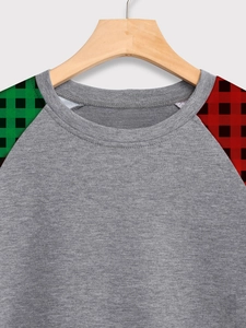 Détail du col rond et manches raglan contrastées avec motif à carreaux rouge et vert sur gris