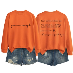 Detailed view of an orange crewneck sweatshirt featuring you are enough back print and denim shorts