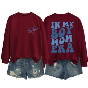 Detail of burgundy Boy Mom Era sweatshirt with blue lettering and distressed denim shorts
