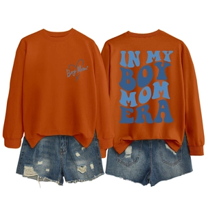 Detail showing the Boy Mom Era graphic print on a bright orange crewneck sweatshirt