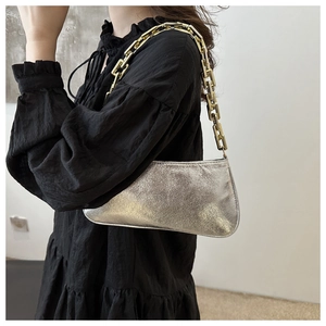 Detail of silver metallic baguette bag with chunky gold chain strap worn by model