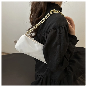 Detail view of a white minimalist shoulder bag featuring a chunky gold chain strap