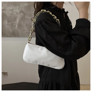 Detail of a white underarm bag featuring a chunky gold chain strap and smooth texture