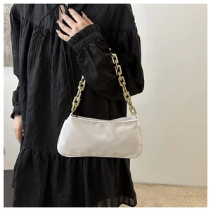 Close-up of a white baguette bag with a chunky gold chain strap on a black dress