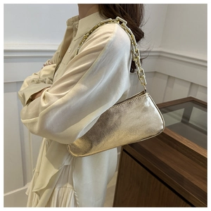 Detail of a metallic gold shoulder bag featuring a chunky square chain strap and texture