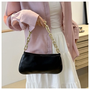 Detail of a black underarm bag with a bold gold chain strap on a stylish model