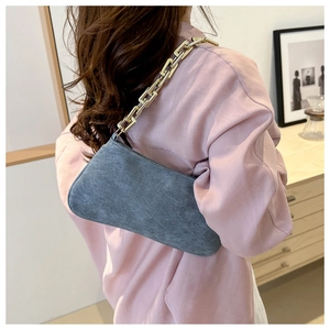 Close-up of grey suede baguette bag with large gold chain strap on shoulder