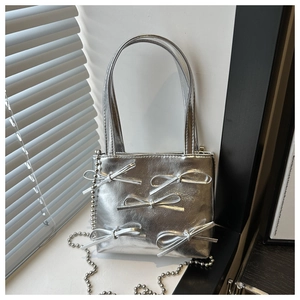 Detailed shot of silver bow handbag with beaded chain strap under artistic lighting