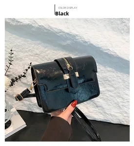 Close-up of black glossy textured crossbody bag with gold metal buckle and flap cover