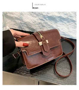 Detail of brown faux leather shoulder bag with gold zipper and metallic buckle on a desk