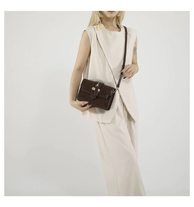 Brown crossbody bag styled with a beige suit, showcasing its compact size and metallic clasp