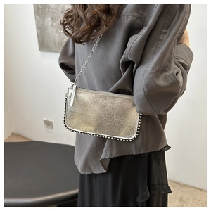 Close-up of silver metallic crossbody bag featuring polished rivets and fine chain strap