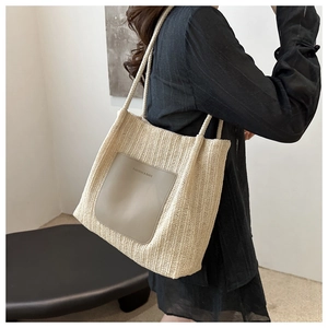 Detail of beige straw tote bag with a grey leather pocket and dual cord shoulder straps