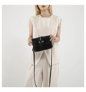 Detail of black crossbody bag with faux crocodile texture and gold metal buckle closure