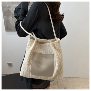 Close-up of beige woven tote bag with brown faux leather pocket and embossed text