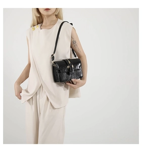 Detail of glossy black patent leather crossbody bag with elegant gold zipper and hardware