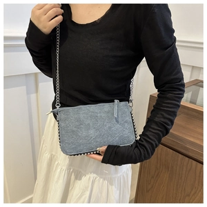 Detail of blue denim textured crossbody bag with silver rivet trim and metal chain strap