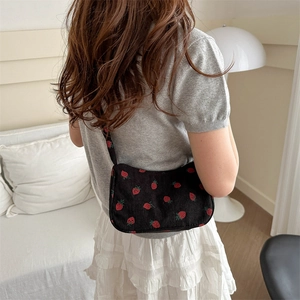 Sac hobo chic en velours noir à motif fraises porté par une femme dans un cadre intérieur