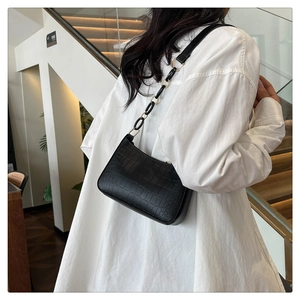 Detail of black crocodile texture underarm bag with gold hardware and chain strap