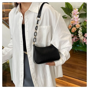 Detail of black crocodile pattern shoulder bag with gold chain strap on a white shirt