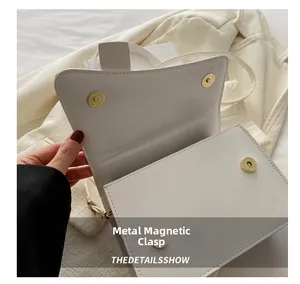 Detail of the golden magnetic snap button on white minimalist leather shoulder bag