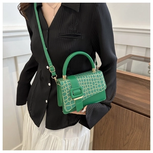 Detail of green crocodile texture shoulder bag with wide decorative buckle on a model