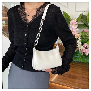 Close-up of white crocodile pattern shoulder bag with golden hardware on a female model