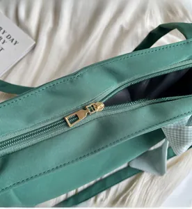 Detailed close-up of a smooth gold metal zipper on a dark green tote bag with bow detail