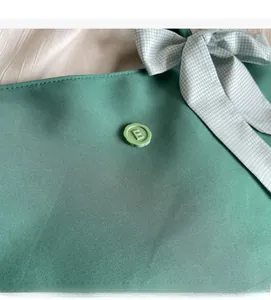 Detail of sage green fabric tote bag featuring a round decorative buckle with embossed letter E
