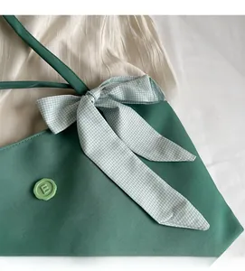 Detail of green leather tote bag featuring a green checkered bow and round letter E badge