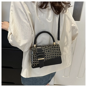 Detail of black leather crossbody bag with golden textured flap and metallic buckle strap
