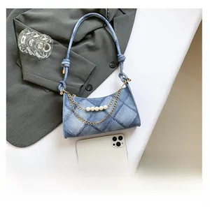 Dettaglio della borsa a mezzaluna in denim blu con ciondoli di perle e tracolla a nodo