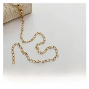 Détail de la bandoulière en chaîne dorée et du fermoir sur un sac à main tissé beige