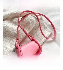Detail of pink faux leather mini saddle bag with adjustable strap on white knit fabric