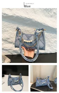 Dettaglio della borsa in denim blu con catena dorata, perle bianche e manico annodato
