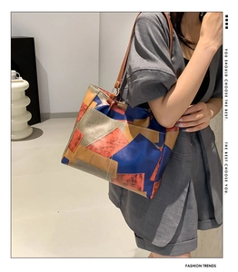 Detail of color-block tote bag with blue and orange leather panels on grey suit