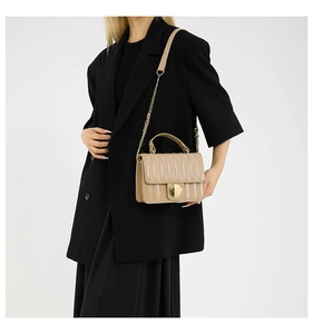 Détail du sac matelassé beige avec fermoir rond doré et bandoulière en chaîne