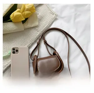 Brown leather saddle bag shown next to a smartphone to demonstrate compact size