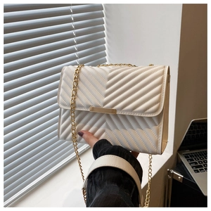 Detail of white quilted crossbody bag with golden chain strap and chevron pattern