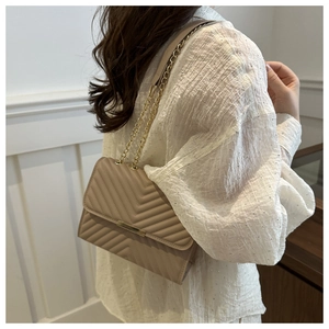 Dettaglio della borsa a tracolla beige trapuntata a V con elegante catena dorata e finiture