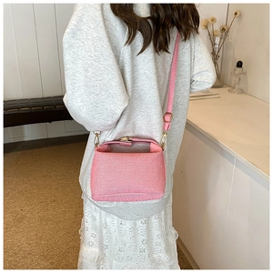 Pink striped fabric crossbody bag with gold buckle detail worn by a model in lifestyle setting