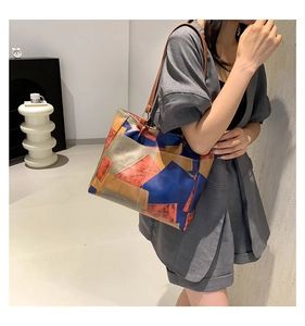 Detail of color-block tote bag showing geometric textures and sturdy leather handles