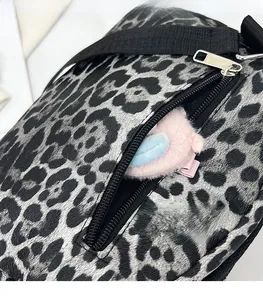 Close-up of leopard print canvas crossbody bag featuring a metal zipper and pink plush charm